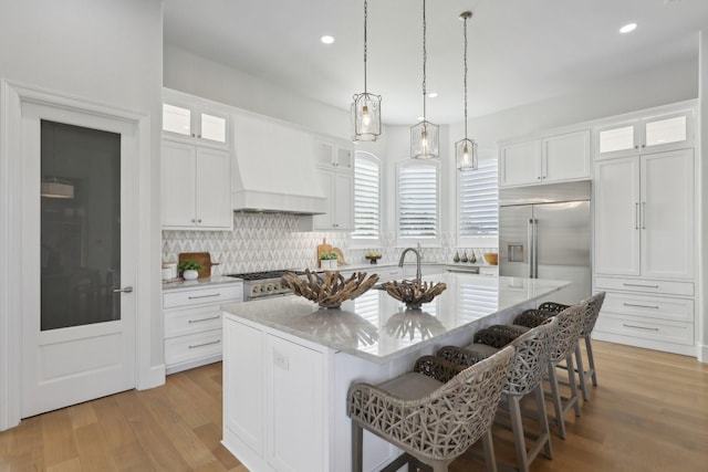 kitchen featuring premium range hood, a kitchen breakfast bar, high end appliances, white cabinets, and a center island with sink