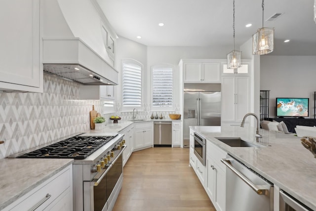 kitchen with built in appliances, sink, hanging light fixtures, and white cabinets