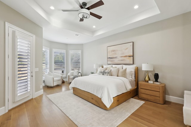 bedroom with access to exterior, light hardwood / wood-style flooring, a raised ceiling, and ceiling fan