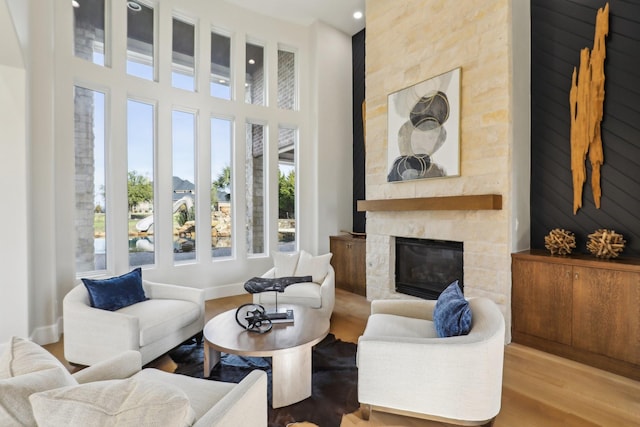 living room with wood-type flooring, a stone fireplace, and a high ceiling