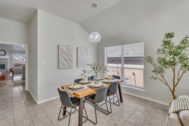 dining room with a tiled fireplace and vaulted ceiling