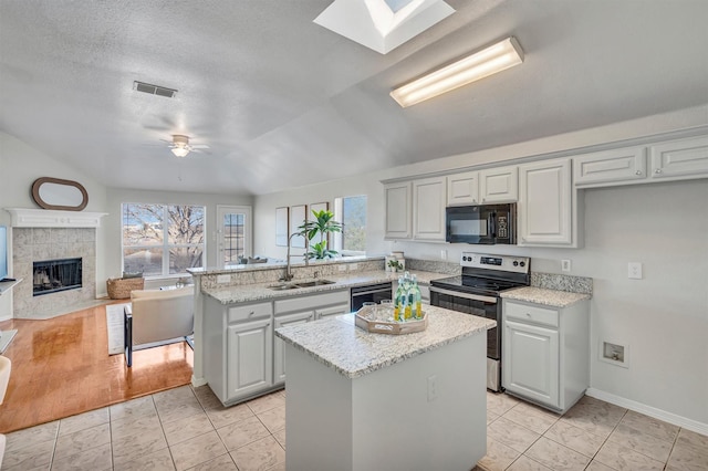 kitchen with sink, a center island, kitchen peninsula, a tiled fireplace, and black appliances