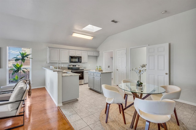 kitchen featuring sink, stainless steel range with electric stovetop, gray cabinetry, vaulted ceiling with skylight, and kitchen peninsula