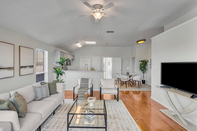 living room with ceiling fan, lofted ceiling, sink, and light hardwood / wood-style flooring