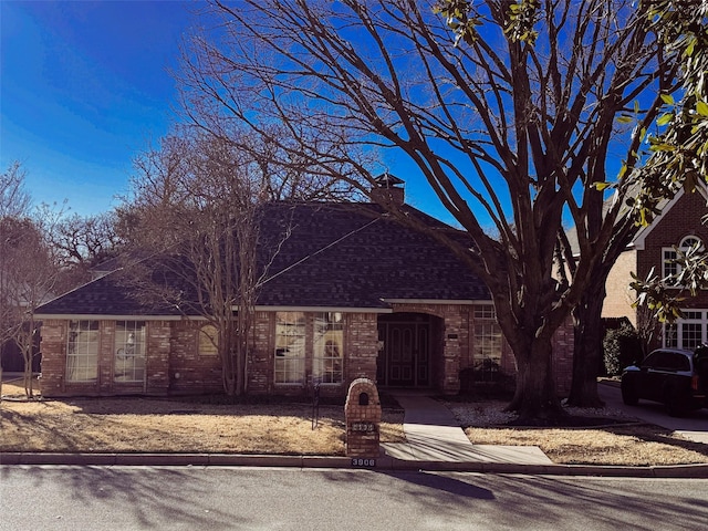 view of front facade featuring brick siding, a chimney, and roof with shingles