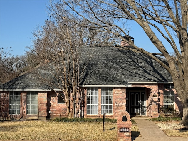 view of front of property with a shingled roof, a front lawn, brick siding, and a chimney