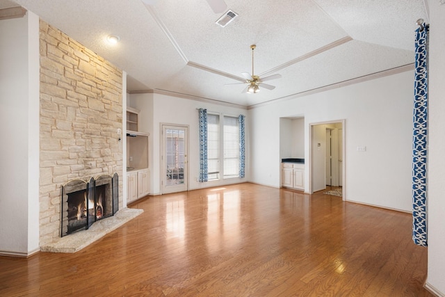 unfurnished living room with visible vents, a raised ceiling, ceiling fan, a textured ceiling, and a stone fireplace