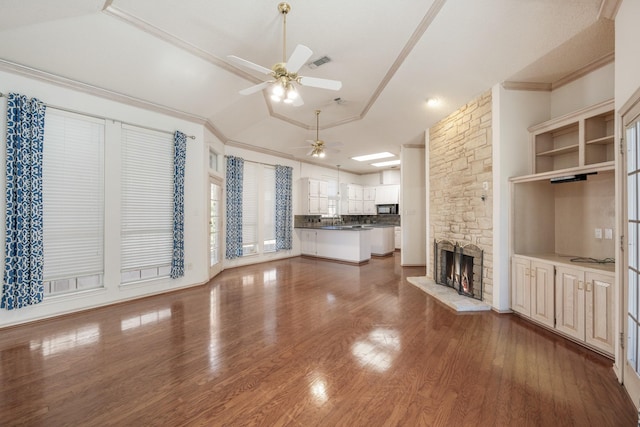 unfurnished living room with ornamental molding, a ceiling fan, a stone fireplace, and wood finished floors