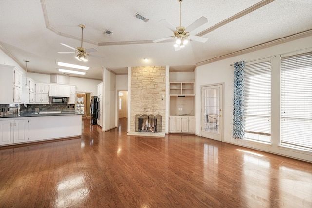 unfurnished living room featuring visible vents, a raised ceiling, a ceiling fan, crown molding, and a fireplace