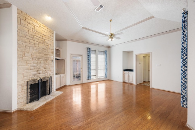 unfurnished living room with a raised ceiling, visible vents, ceiling fan, a stone fireplace, and a textured ceiling