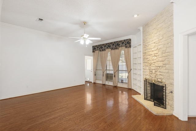 unfurnished living room featuring dark wood finished floors, crown molding, visible vents, a stone fireplace, and baseboards