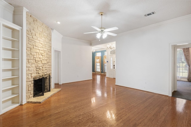 unfurnished living room featuring crown molding, ceiling fan with notable chandelier, hardwood / wood-style floors, a textured ceiling, and a stone fireplace