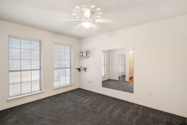 spare room featuring baseboards, a ceiling fan, dark colored carpet, and a textured ceiling