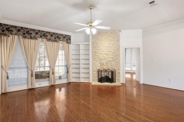 unfurnished living room with crown molding, built in features, ceiling fan, hardwood / wood-style floors, and a stone fireplace