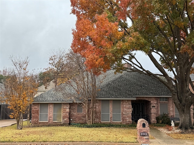 view of front facade featuring a shingled roof, brick siding, and a front lawn