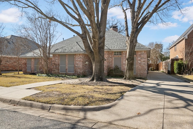 ranch-style home with a shingled roof, fence, a chimney, and brick siding