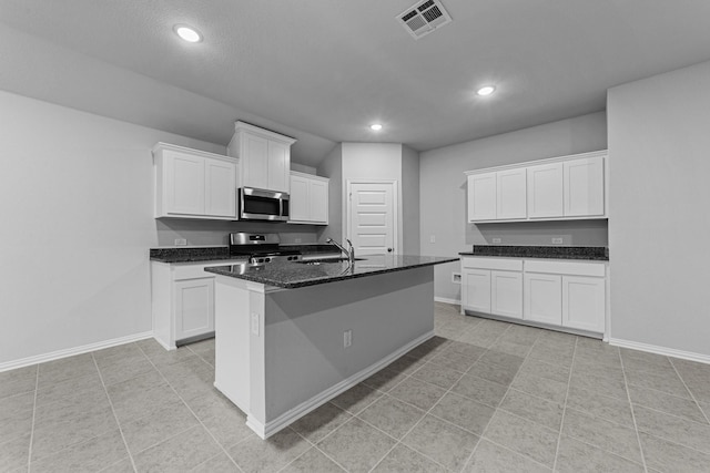 kitchen featuring sink, white cabinets, dark stone counters, stainless steel appliances, and a center island with sink