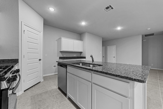 kitchen featuring sink, a kitchen island with sink, white cabinets, stainless steel dishwasher, and dark stone counters