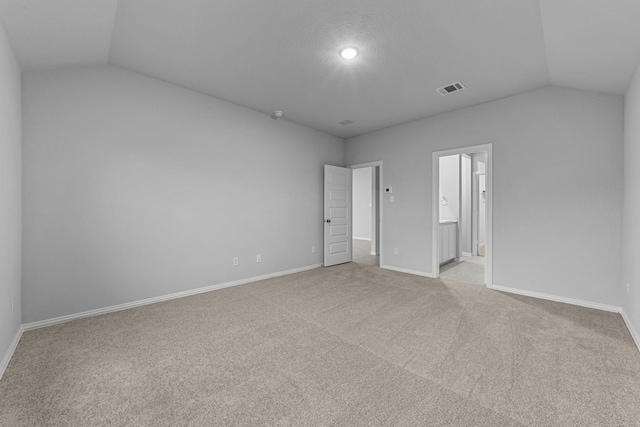 unfurnished bedroom with vaulted ceiling, light carpet, and ensuite bath