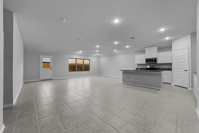 kitchen featuring light tile patterned flooring, sink, white cabinets, stainless steel appliances, and a center island with sink