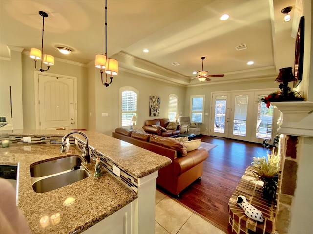 kitchen featuring decorative light fixtures, sink, ornamental molding, light stone counters, and a tray ceiling