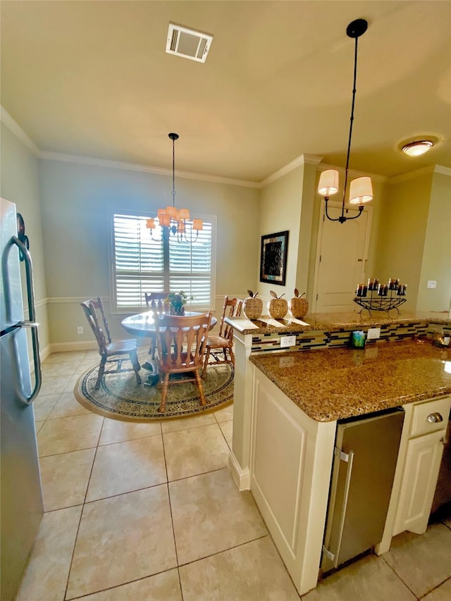 kitchen with an inviting chandelier, white cabinetry, decorative light fixtures, stainless steel fridge, and stone counters