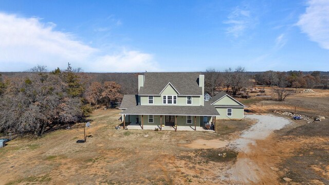 view of front of property featuring covered porch, driveway, a chimney, and a shingled roof