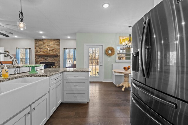 kitchen featuring a stone fireplace, white cabinetry, dark hardwood / wood-style flooring, hanging light fixtures, and light stone counters