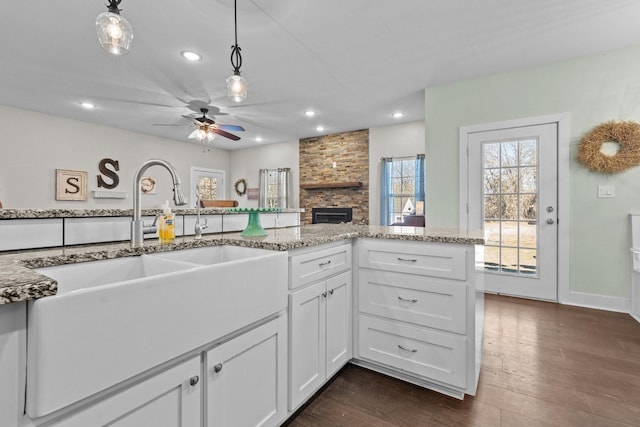 kitchen with white cabinets, a stone fireplace, recessed lighting, a sink, and hanging light fixtures