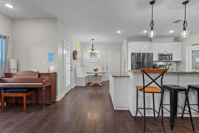 kitchen featuring visible vents, white cabinets, a kitchen breakfast bar, stainless steel appliances, and light stone counters