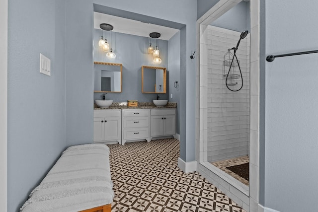 bathroom featuring tiled shower, double vanity, a sink, and baseboards