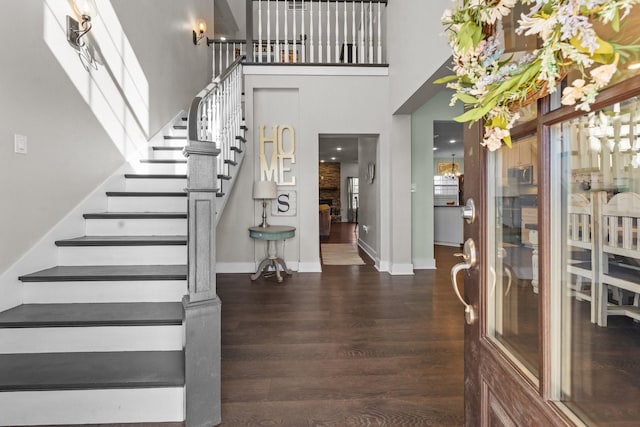 foyer with dark wood-style flooring, baseboards, a towering ceiling, and stairs