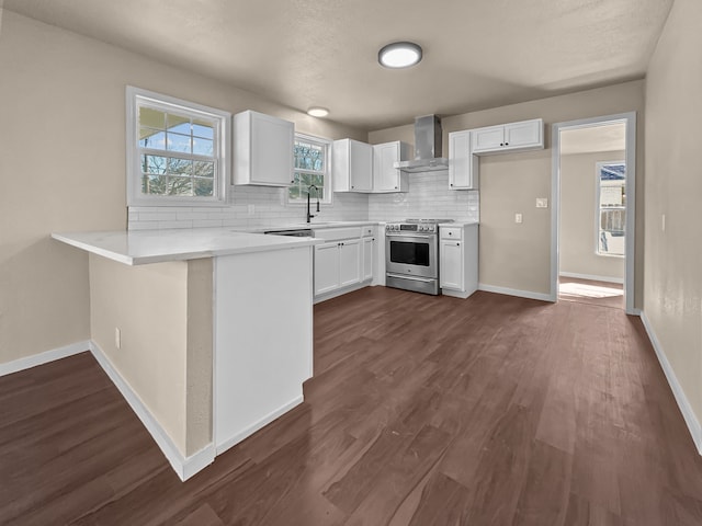 kitchen with wall chimney range hood, stainless steel stove, decorative backsplash, and white cabinets