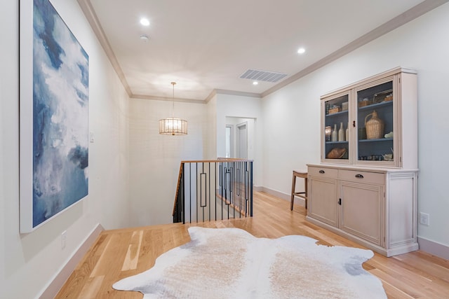 hallway featuring a notable chandelier, an upstairs landing, visible vents, ornamental molding, and light wood finished floors