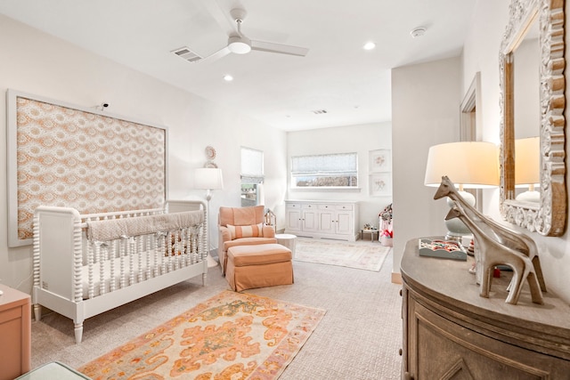 bedroom with a crib, light colored carpet, and ceiling fan