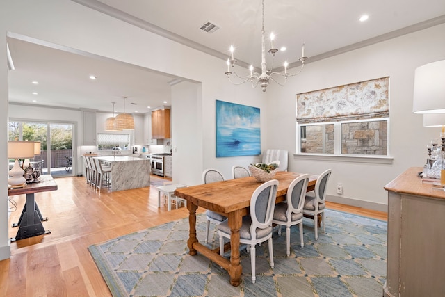 dining space featuring an inviting chandelier, ornamental molding, and light wood-type flooring