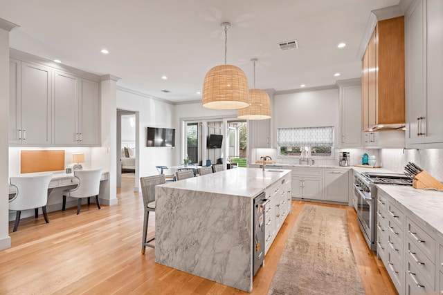 kitchen with light stone counters, high end range, a center island with sink, pendant lighting, and backsplash