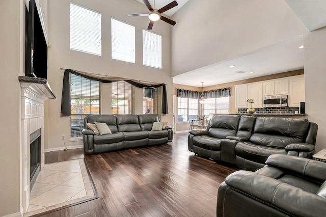 living room with ceiling fan, a tiled fireplace, and light hardwood / wood-style floors