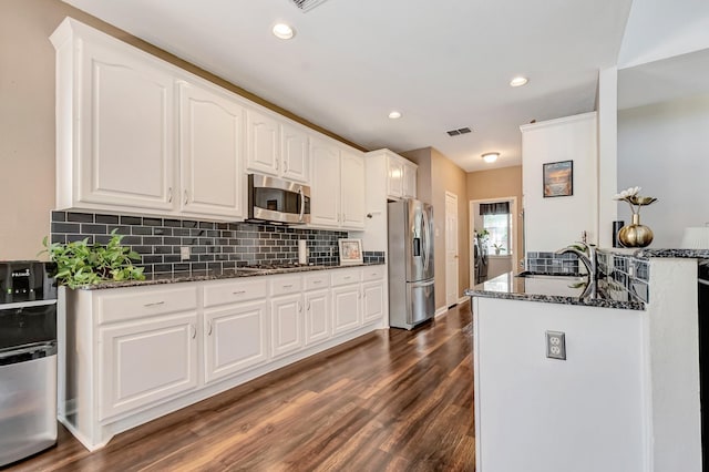 kitchen with appliances with stainless steel finishes, sink, dark stone countertops, white cabinets, and decorative backsplash