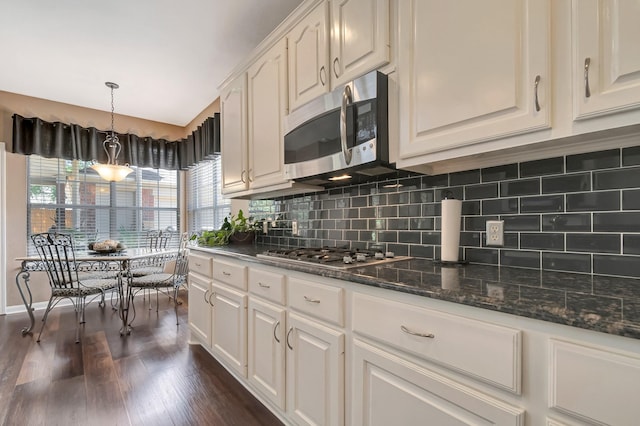 kitchen featuring dark wood-type flooring, appliances with stainless steel finishes, pendant lighting, dark stone counters, and backsplash