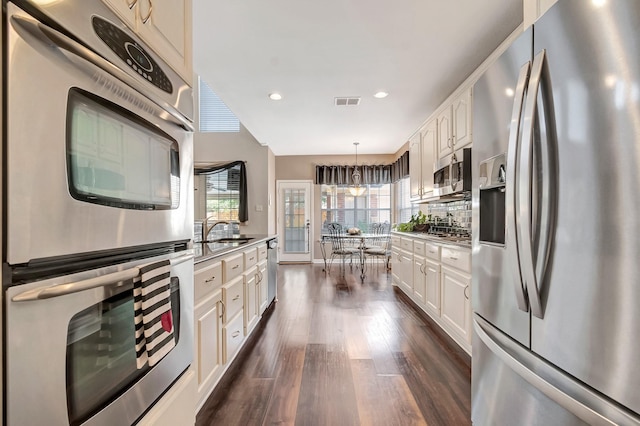 kitchen featuring tasteful backsplash, appliances with stainless steel finishes, hanging light fixtures, and white cabinets