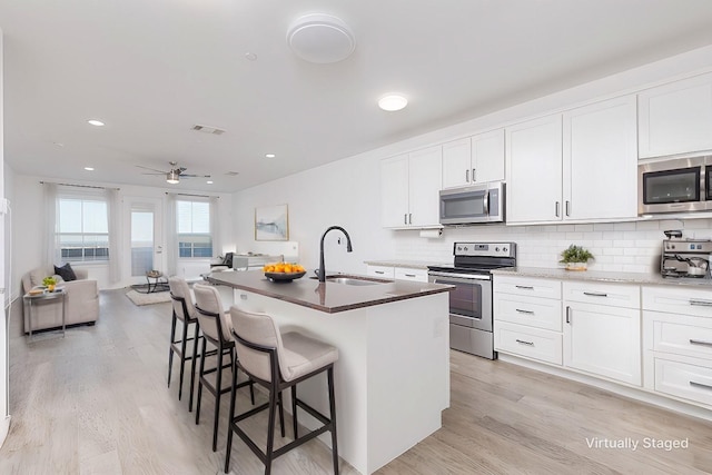 kitchen featuring a center island with sink, white cabinets, stainless steel appliances, a kitchen bar, and a sink