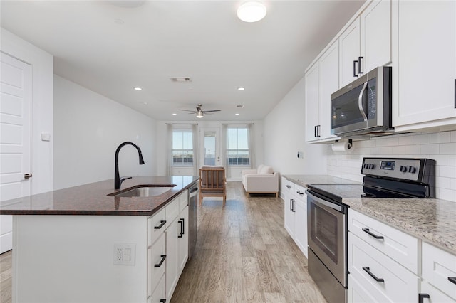 kitchen with stainless steel appliances, a sink, white cabinets, light stone countertops, and a center island with sink