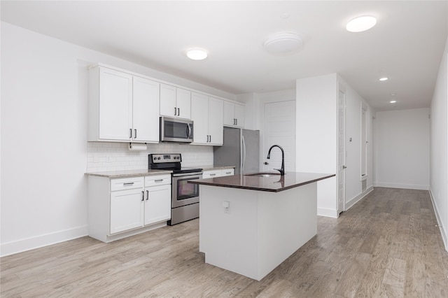 kitchen featuring tasteful backsplash, a center island with sink, appliances with stainless steel finishes, white cabinetry, and a sink