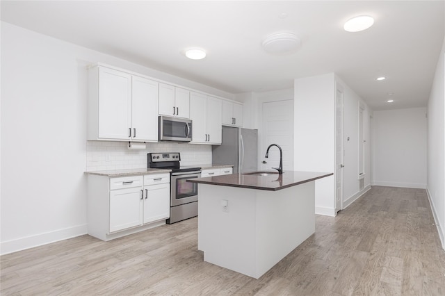 kitchen with a center island with sink, tasteful backsplash, appliances with stainless steel finishes, white cabinets, and a sink