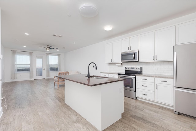 kitchen featuring a center island with sink, appliances with stainless steel finishes, open floor plan, white cabinets, and a sink