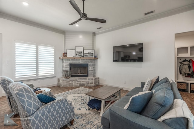 living room featuring crown molding, ceiling fan, a stone fireplace, and hardwood / wood-style floors