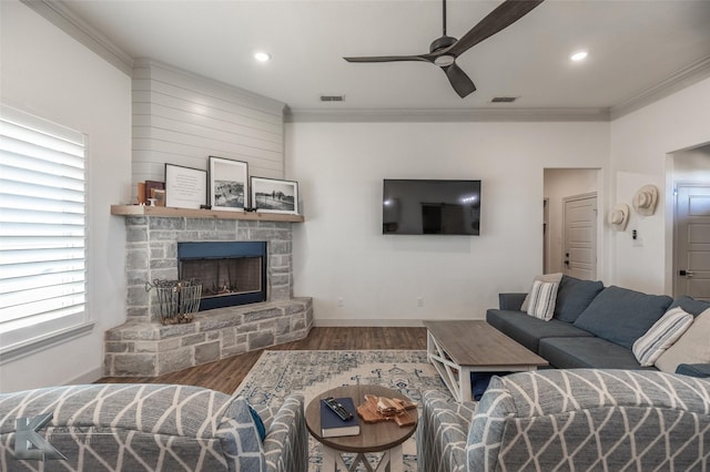 living room with ceiling fan, ornamental molding, a stone fireplace, and hardwood / wood-style floors