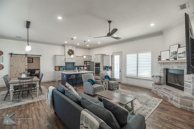 living room featuring crown molding, a fireplace, a barn door, and dark hardwood / wood-style flooring