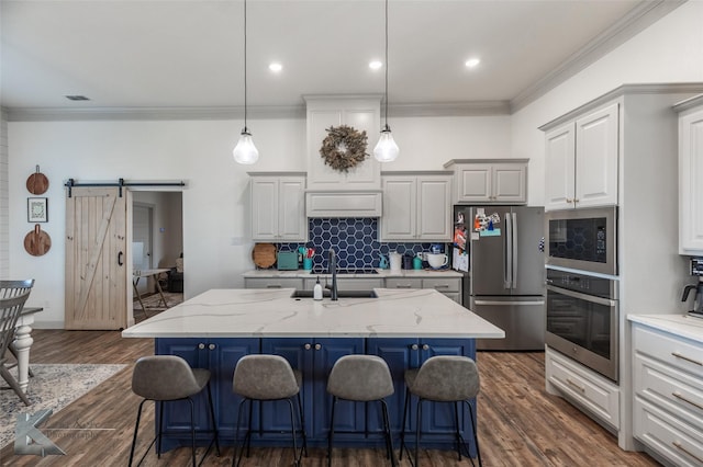 kitchen with appliances with stainless steel finishes, a kitchen island with sink, a kitchen breakfast bar, light stone counters, and a barn door